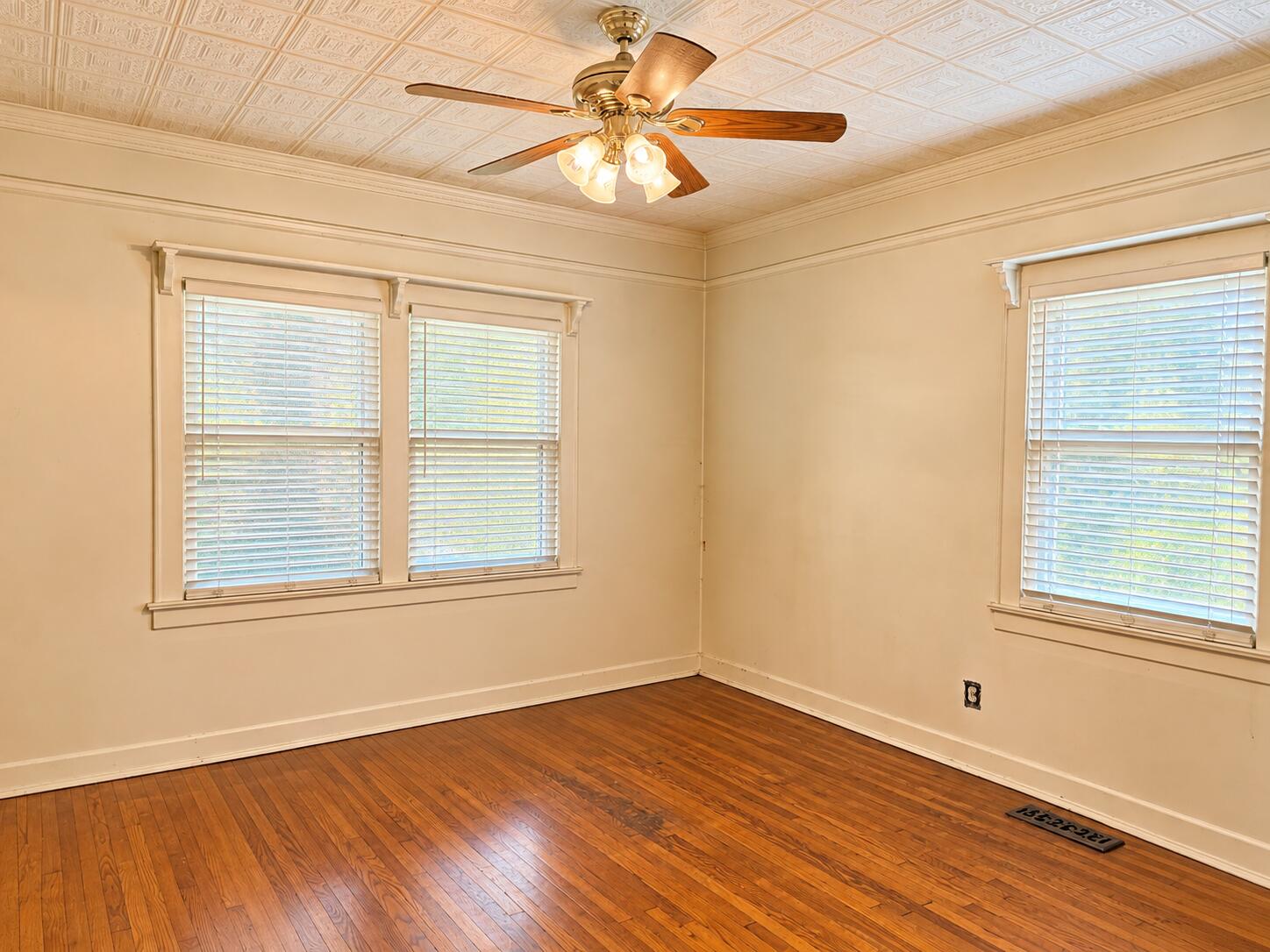 Empty room with hardwood floors, a patterned ceiling, ceiling fan, and three windows with blinds.