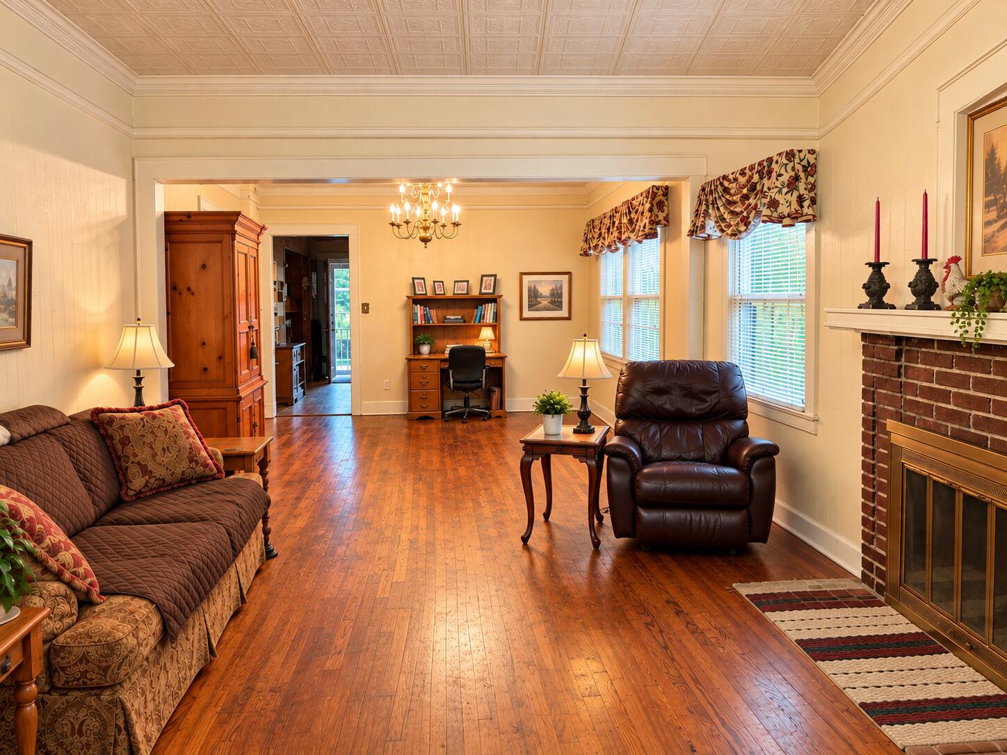 Living room with polished hardwood floors, patterned ceiling, leather seating, and a brick fireplace.