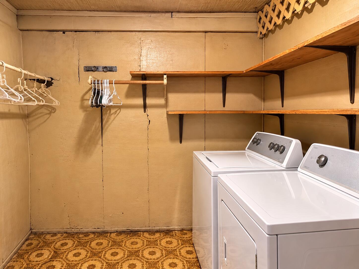 Laundry room with a washer and dryer beneath long wooden storage shelves.