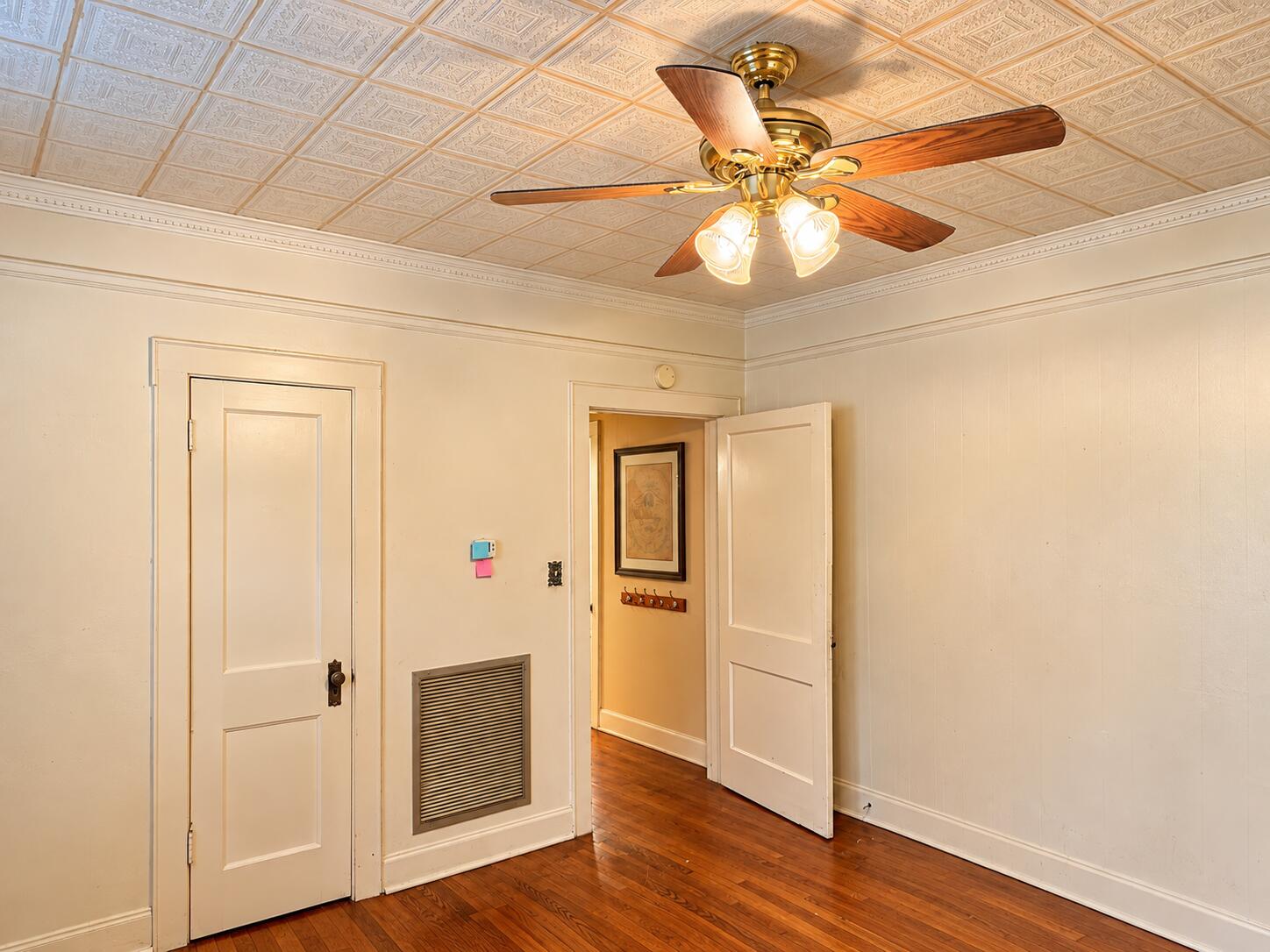 Empty room with polished hardwood floors, a patterned ceiling, and a brass ceiling fan.