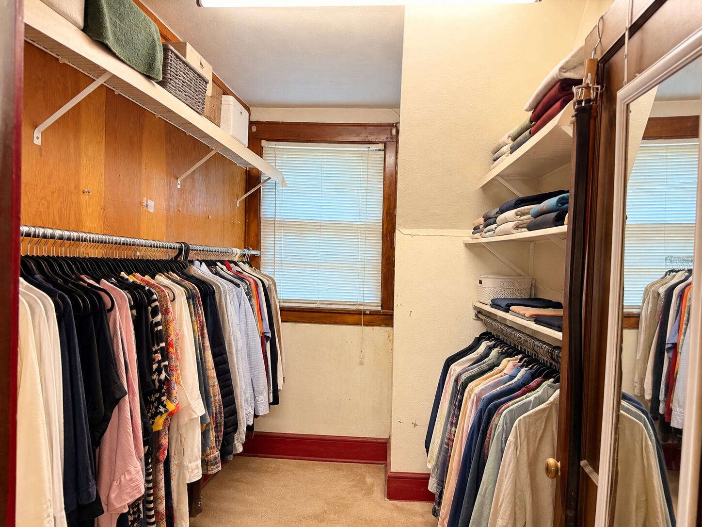 Walk-in closet with clothing racks on both sides, folded linens, and a mirrored sliding door.