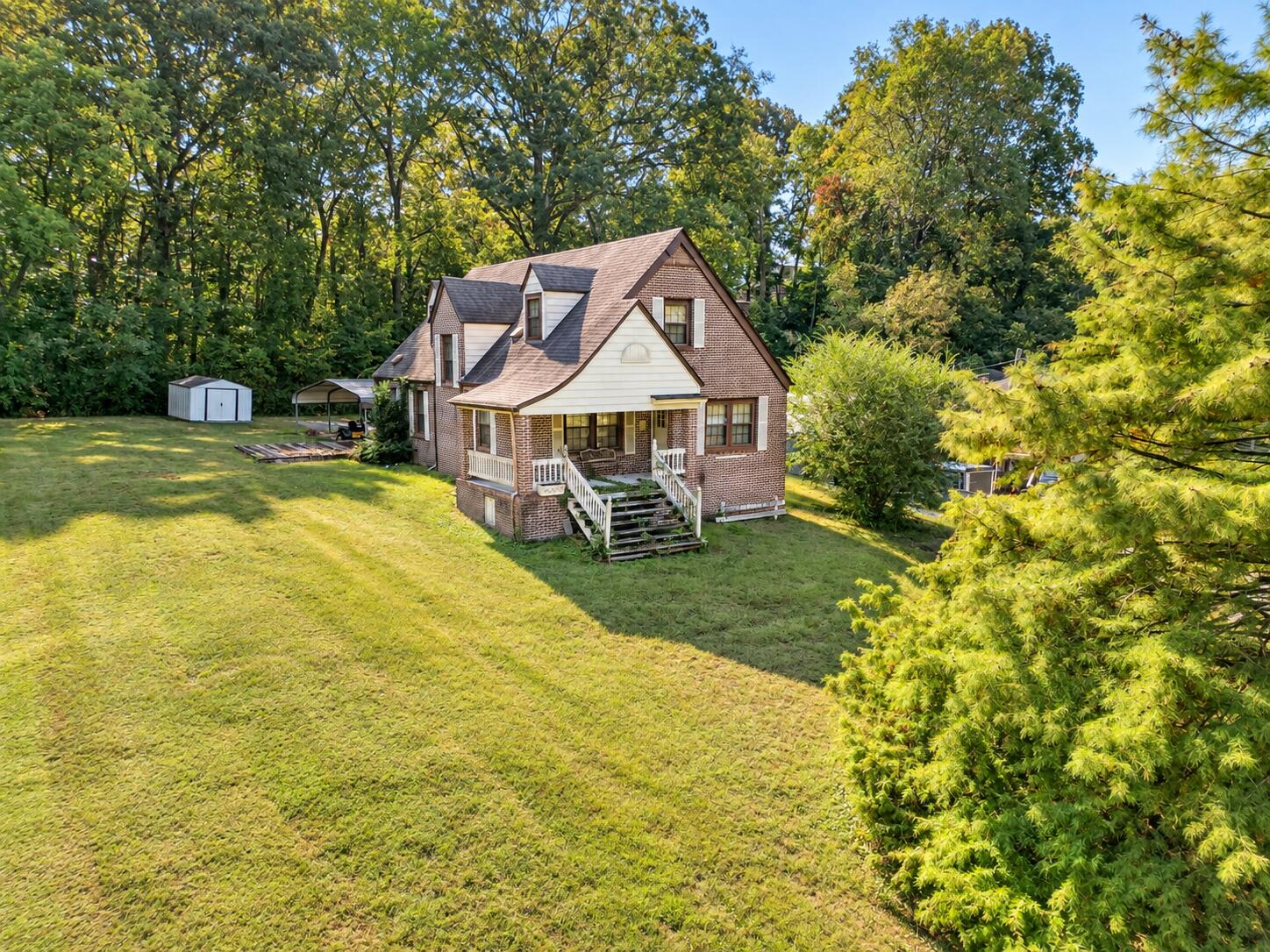 Aerial view of a brick house with a front porch, broad lawn, and mature trees.