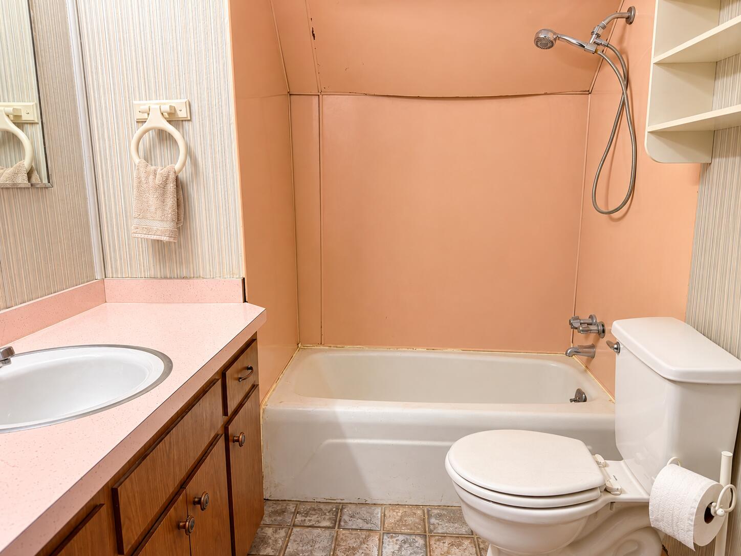 Bathroom with a white tub and shower, wood vanity, toilet, and peach-colored walls.
