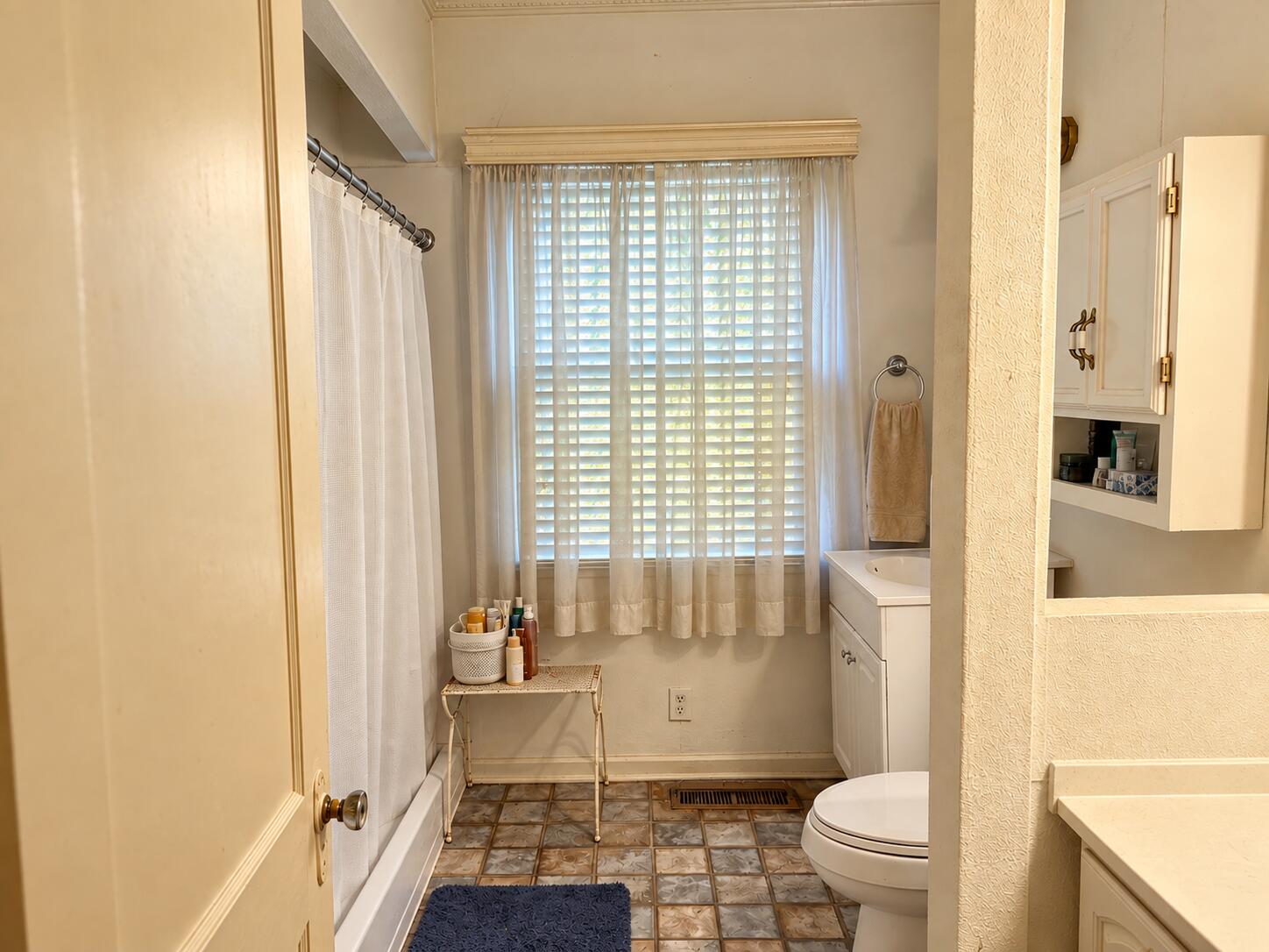 Bathroom with a curtained tub and shower, white vanity, and large window with blinds.
