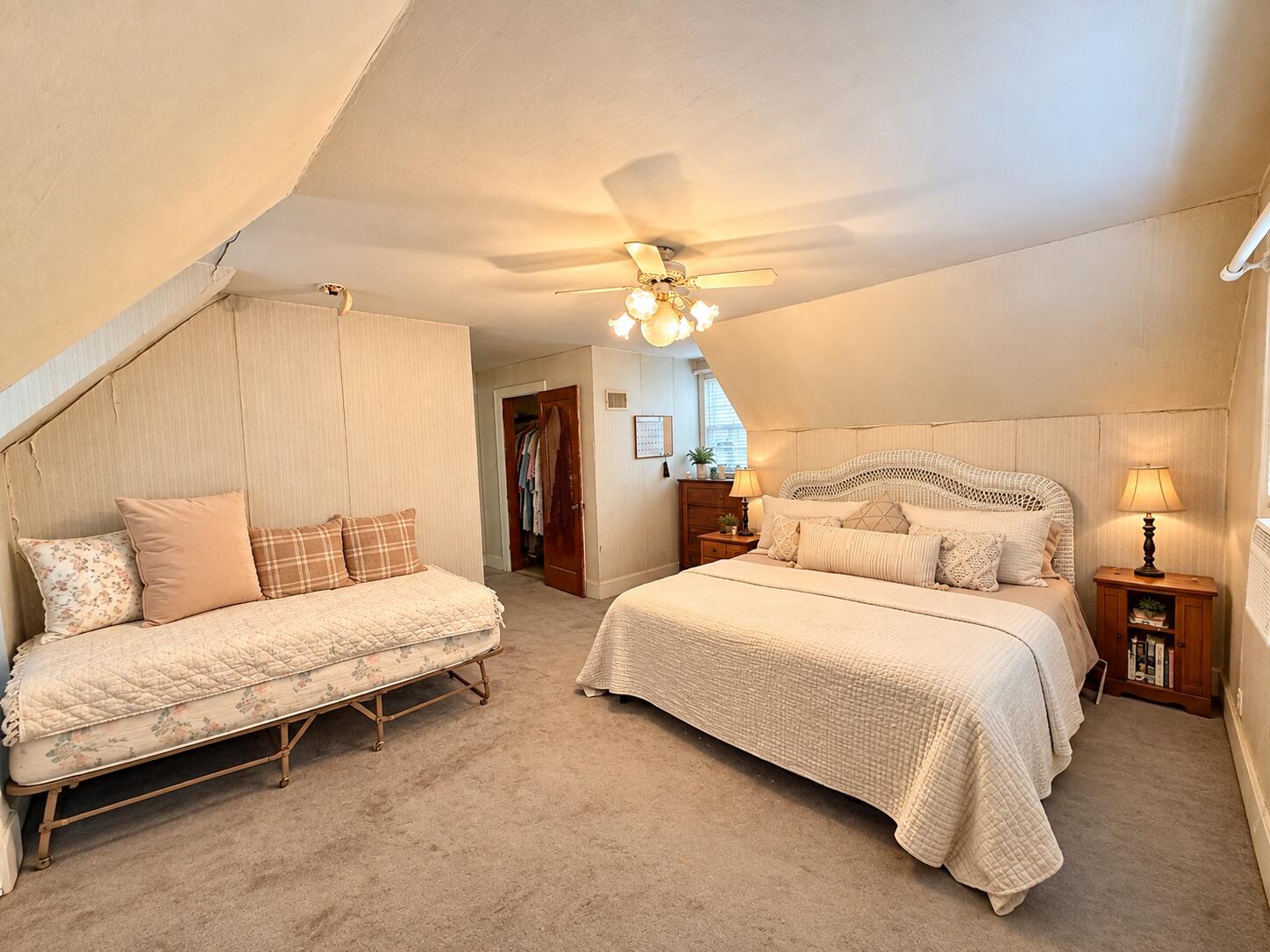 Attic bedroom with a large bed, daybed, sloped ceilings, and ceiling fan.