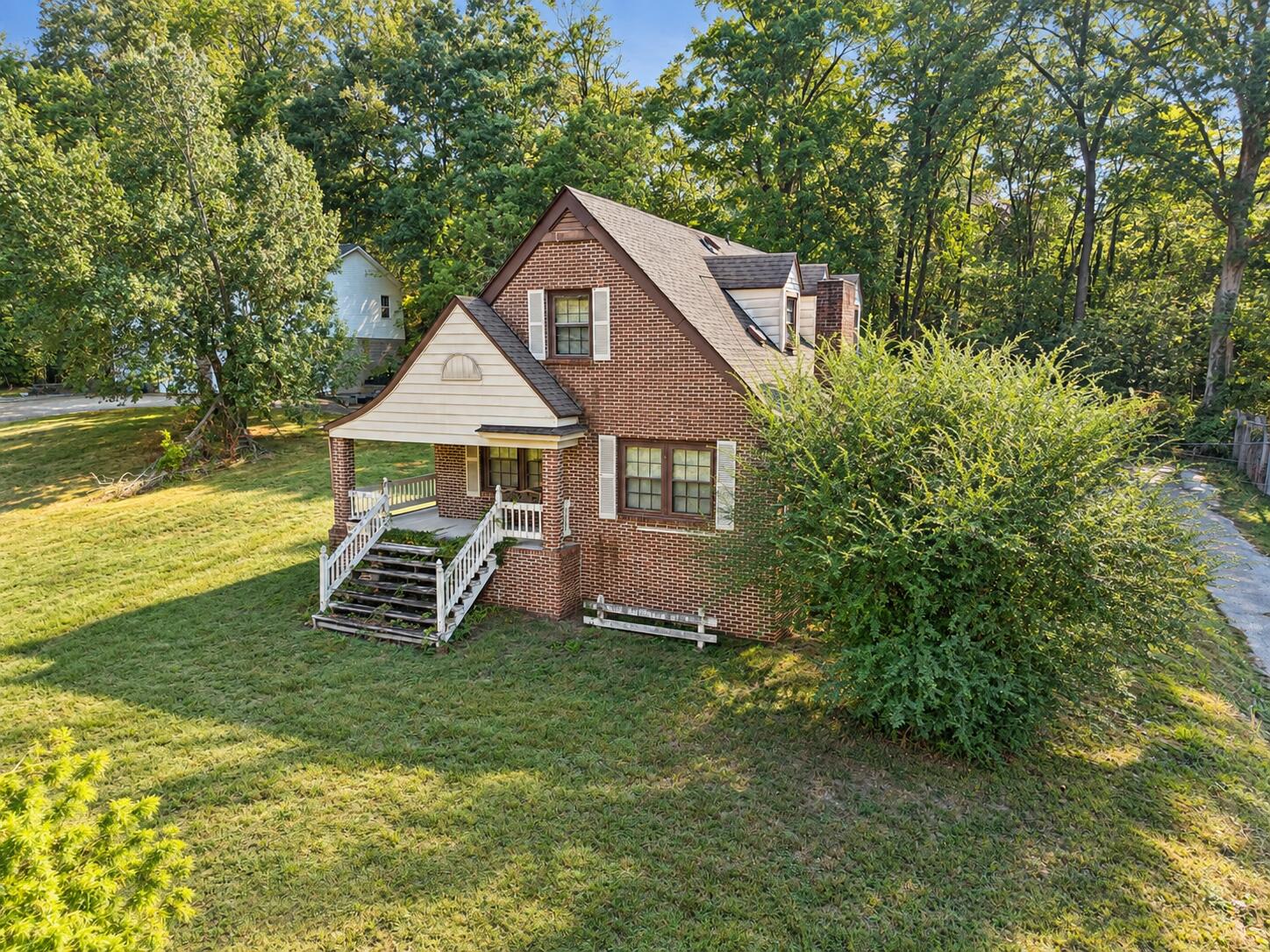 Red-brick house with a white-railed porch on a wooded lot.