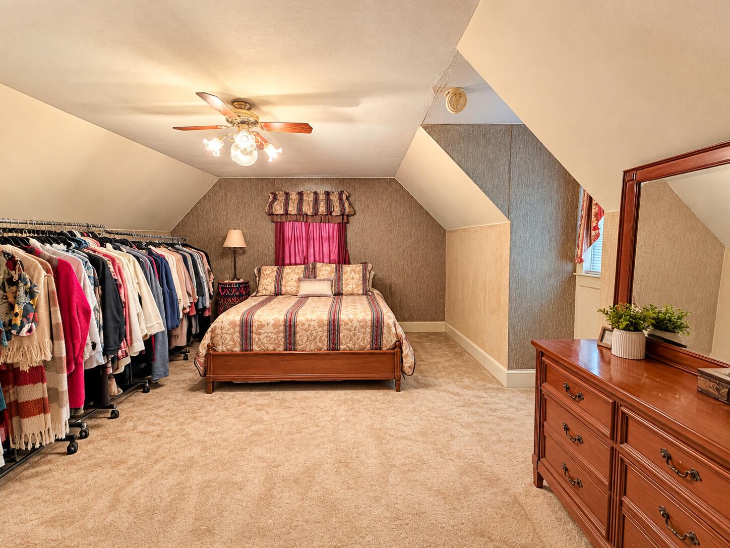 Attic bedroom with a bed, sloped ceilings, clothing racks, and a wooden dresser with mirror.