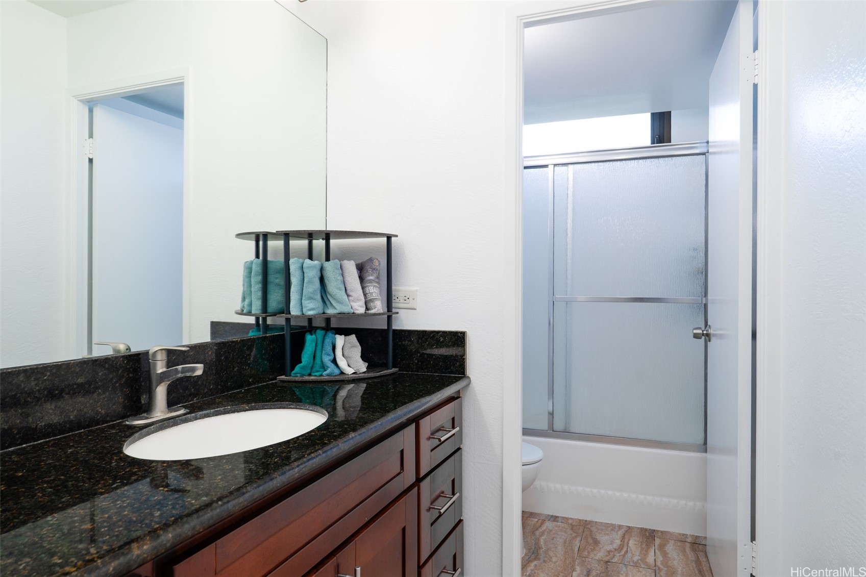 Bathroom with granite vanity and sink, dark wood cabinets, and frosted-glass tub-shower doors.
