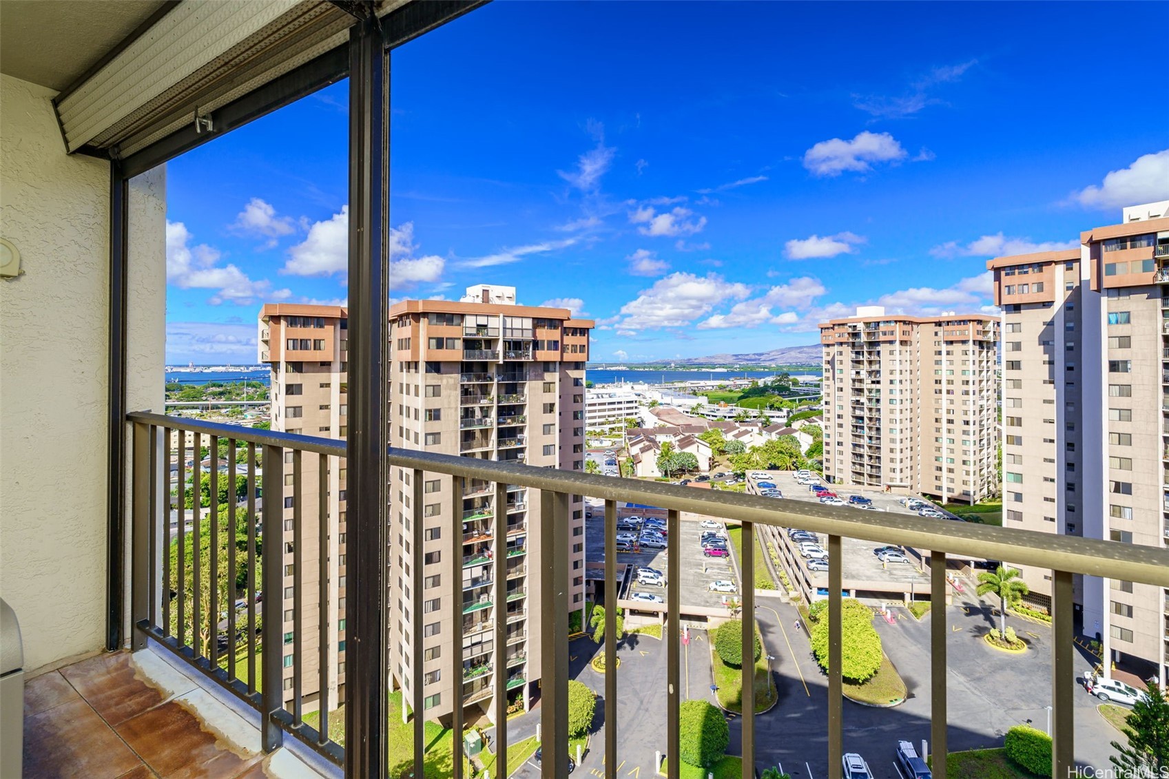 High-rise balcony overlooking neighboring towers, blue water, and distant hills.