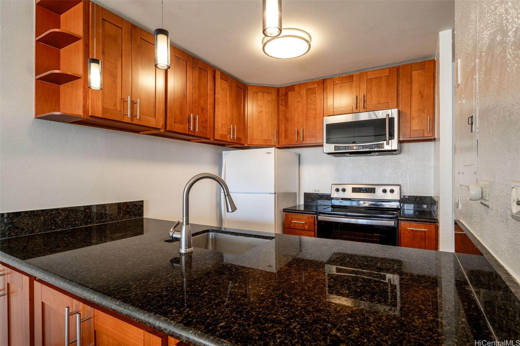 Kitchen with warm wood cabinets, dark granite counters, a peninsula sink, and stainless-steel range and microwave.