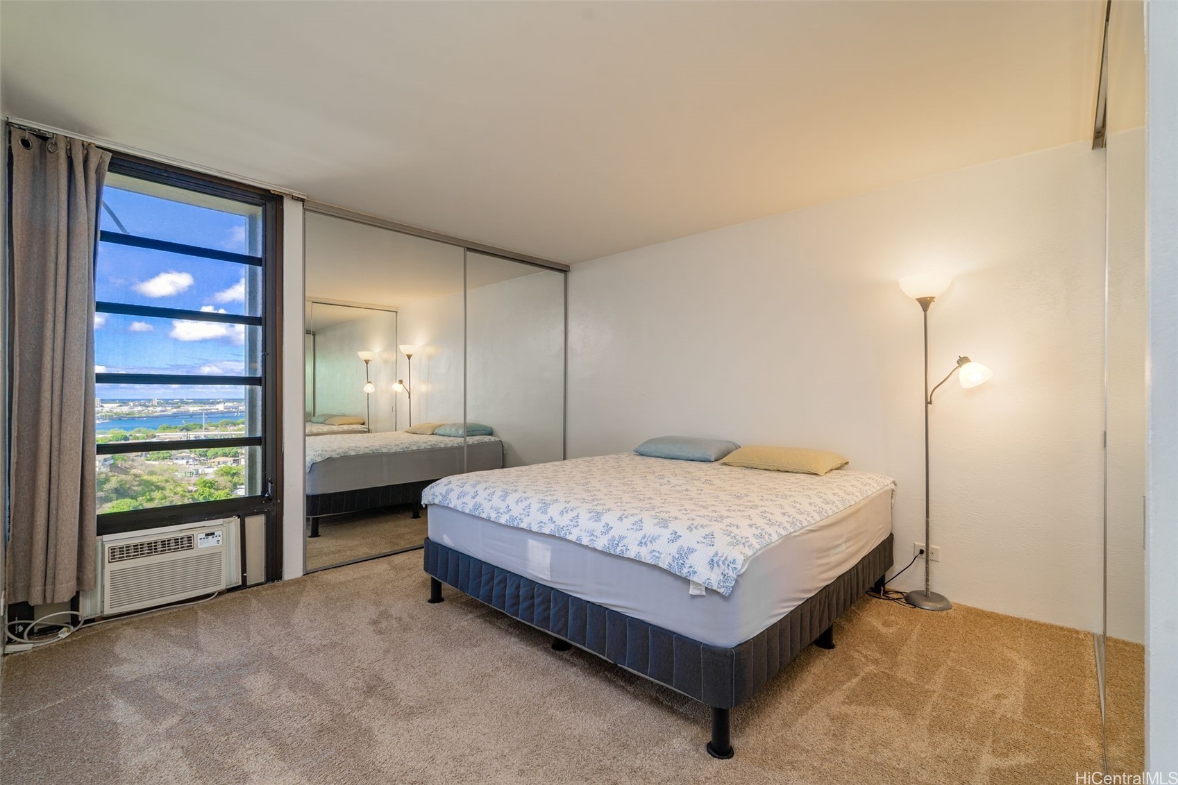 Bedroom with mirrored closet doors and a window overlooking water and buildings.