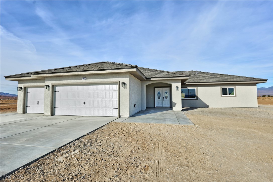 Single-story stucco home with two garage doors and a wide concrete driveway on a bare desert lot.
