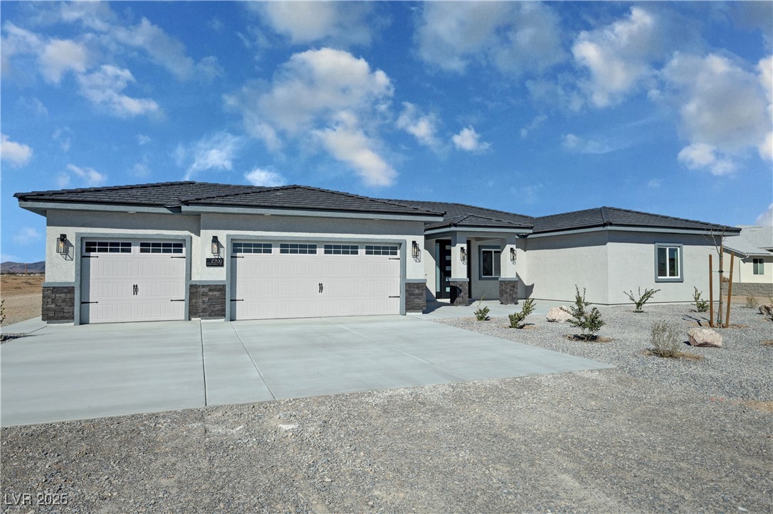 Single-story stucco home with a broad two-car garage, gravel landscaping, and distant hills.
