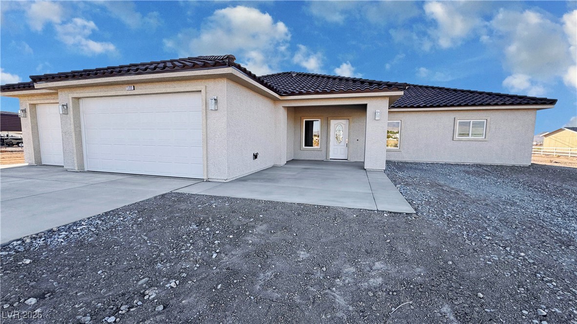 Single-story stucco home with a tiled roof, two-car garage, and gravel yard.