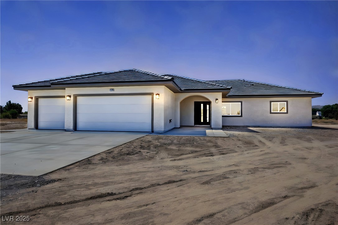 Single-story stucco home with a three-car garage and unfinished dirt yard at dusk.