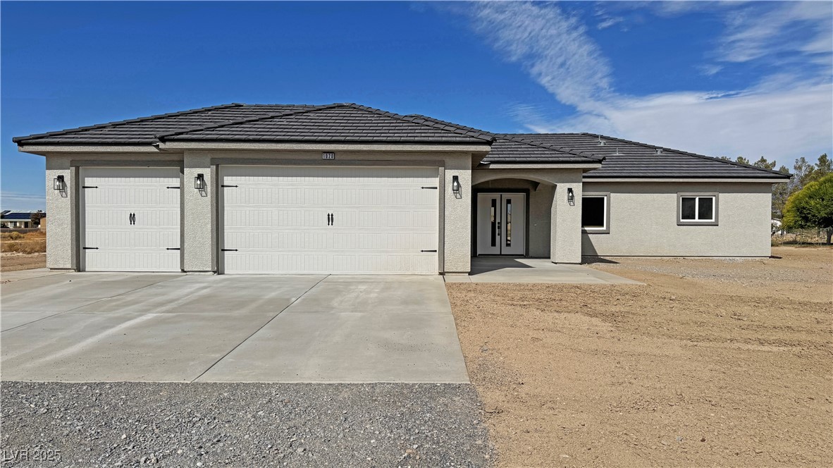 Single-story stucco home with a dark tiled roof, three-car garage, and wide concrete driveway.
