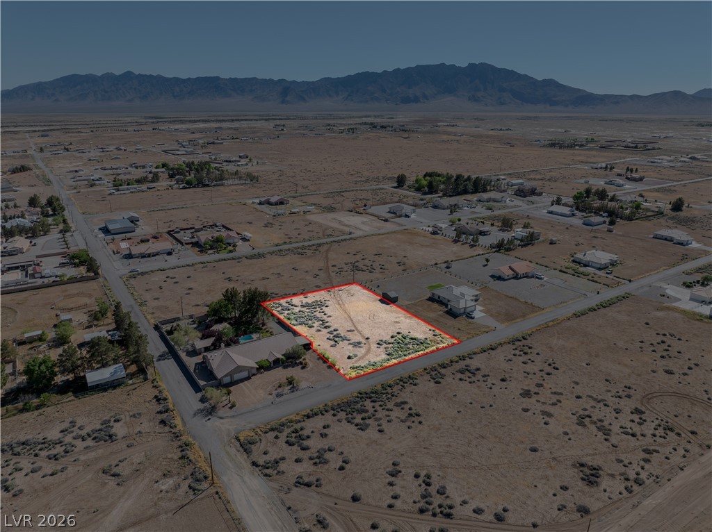 Aerial view of a vacant lot outlined in red, with Pahrump homes and mountains beyond.