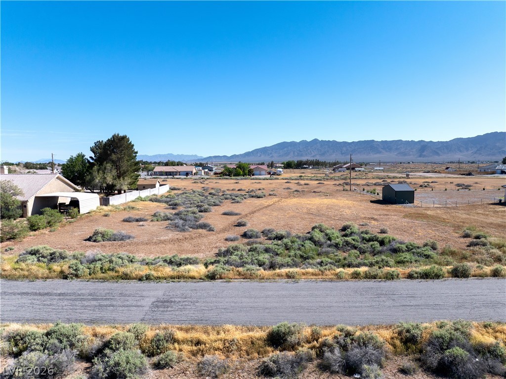 Dry, scrub-covered lot beside a paved road, with a mountain range on the horizon.