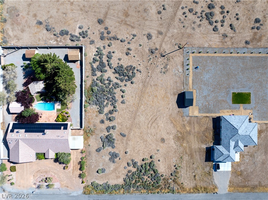 Aerial view of a Pahrump home with a swimming pool and rooftop solar panels beside open desert land.
