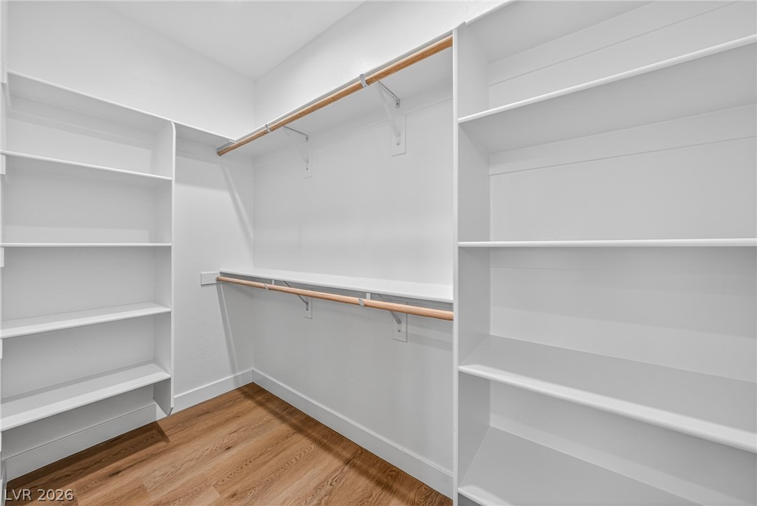 Walk-in closet with built-in white shelving, wooden hanging rods, and wood-look flooring.