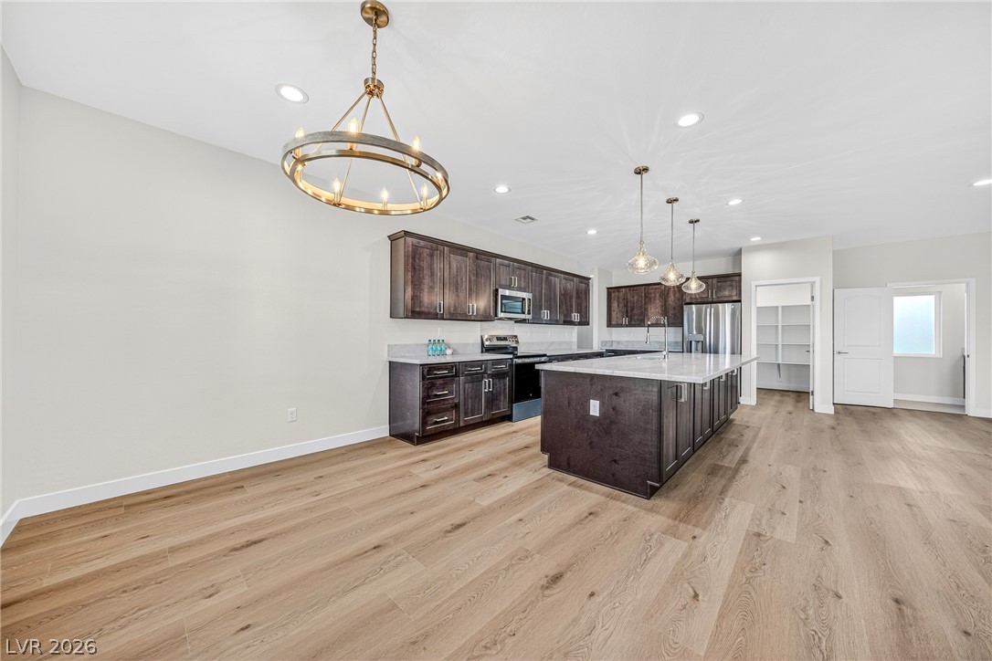Vacant kitchen with a large island, dark cabinetry, stainless steel appliances, and light wood flooring.