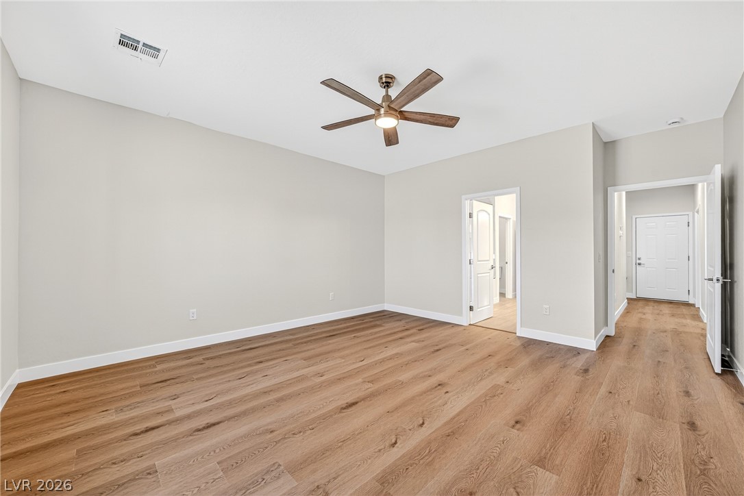 Vacant living room with wide-plank wood flooring and a wood-blade ceiling fan.