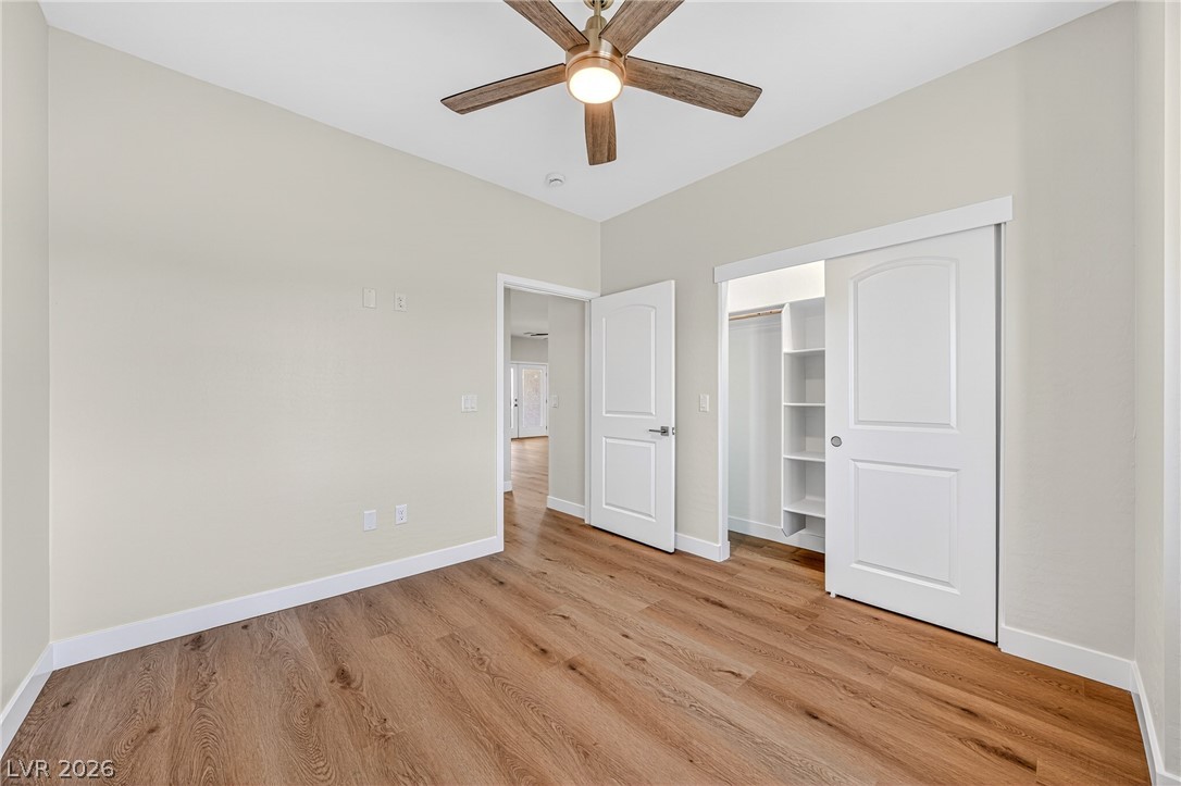 Empty bedroom with wood-look flooring, a ceiling fan, and an open closet with built-in shelves.