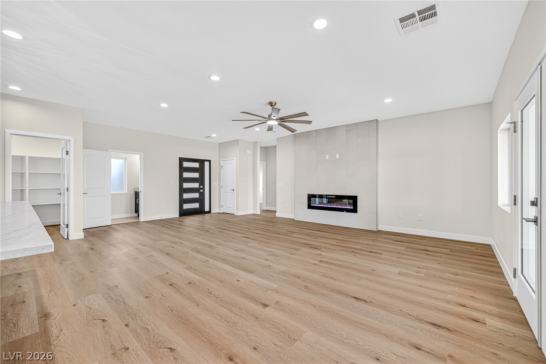 Vacant living room with a tiled fireplace wall, wood-look flooring, and ceiling fan.