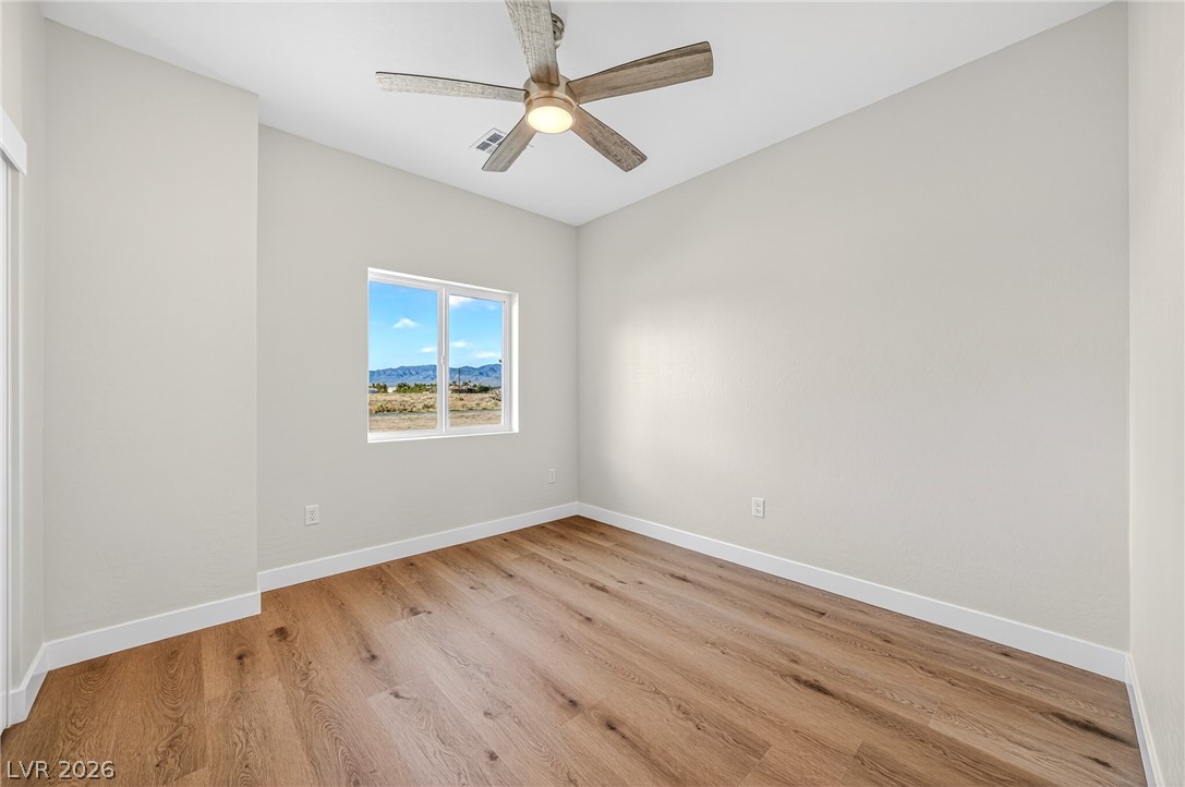 Empty room with wood-look flooring, a ceiling fan, and a window overlooking distant mountains.