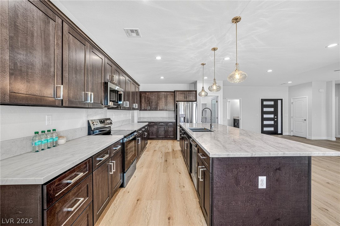 Kitchen with dark wood cabinets, stainless appliances, and a large marble-look island beneath pendant lights.