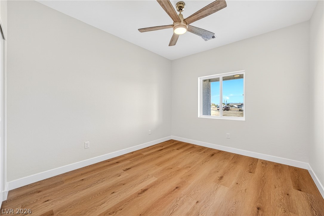 Empty bedroom with wood flooring, a ceiling fan, and a window overlooking the yard.