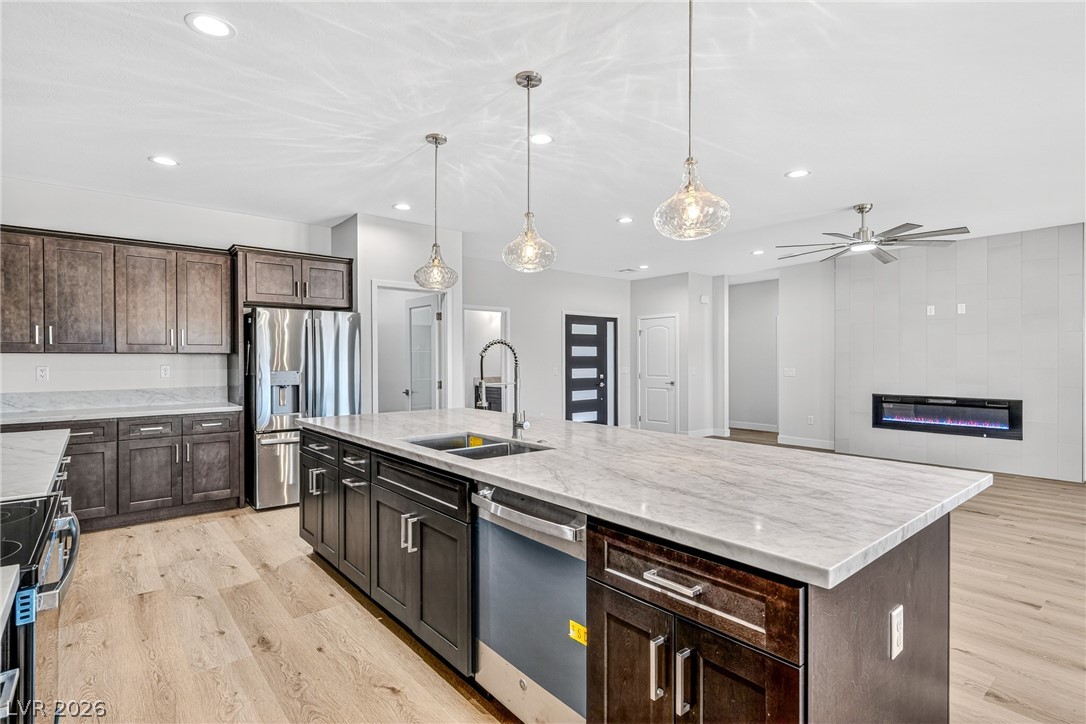 Open-plan kitchen with a large marble-look island, dark cabinetry, stainless appliances, and an adjoining electric fireplace.