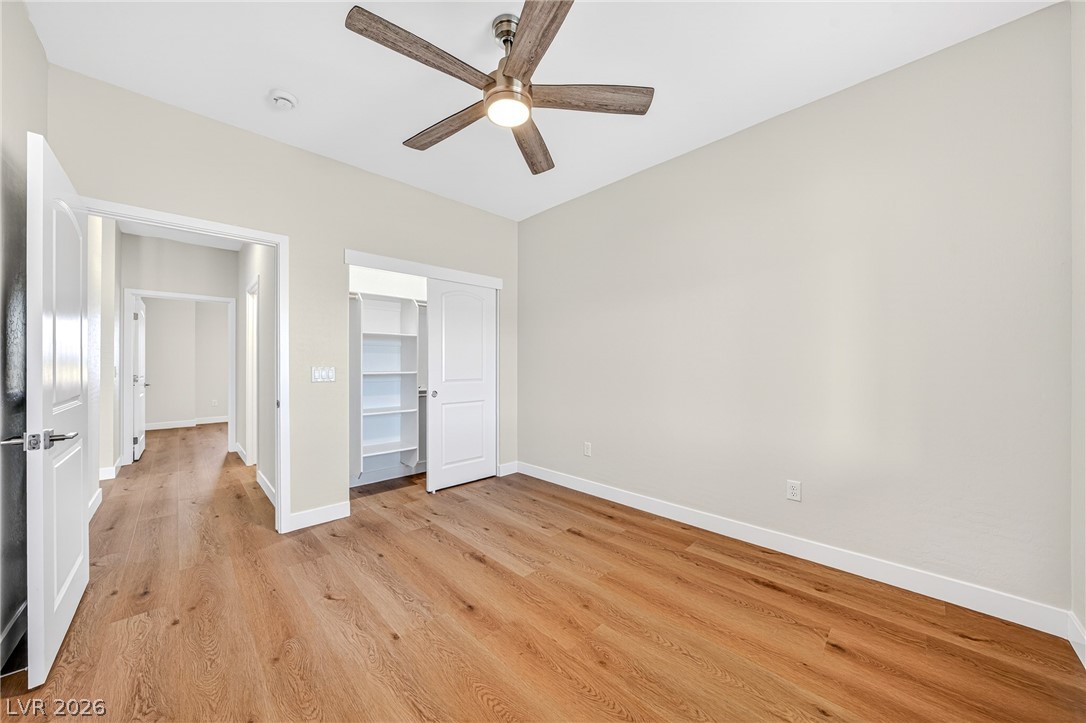 Empty bedroom with warm wood floors, a ceiling fan, and an open closet with built-in shelves.