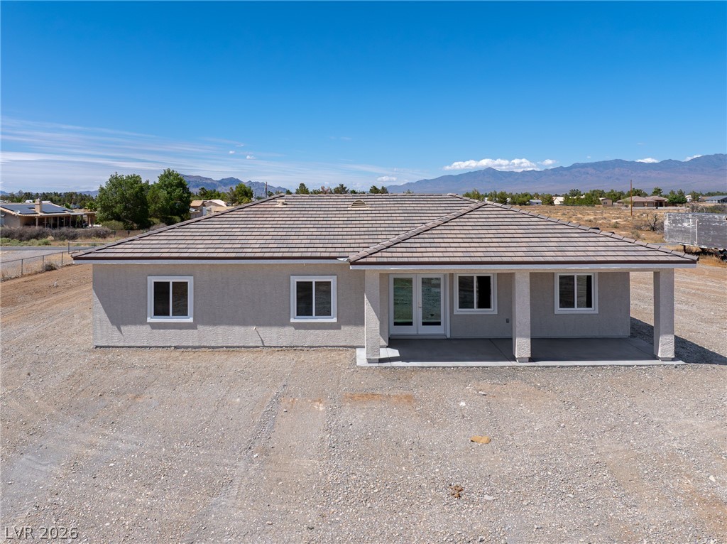 Single-story gray home with a broad tiled roof and covered entry on a gravel lot, with mountains behind.