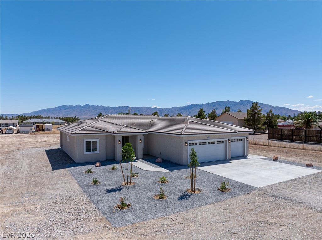 Single-story gray home with two garage doors, a wide driveway, and mountains behind it.