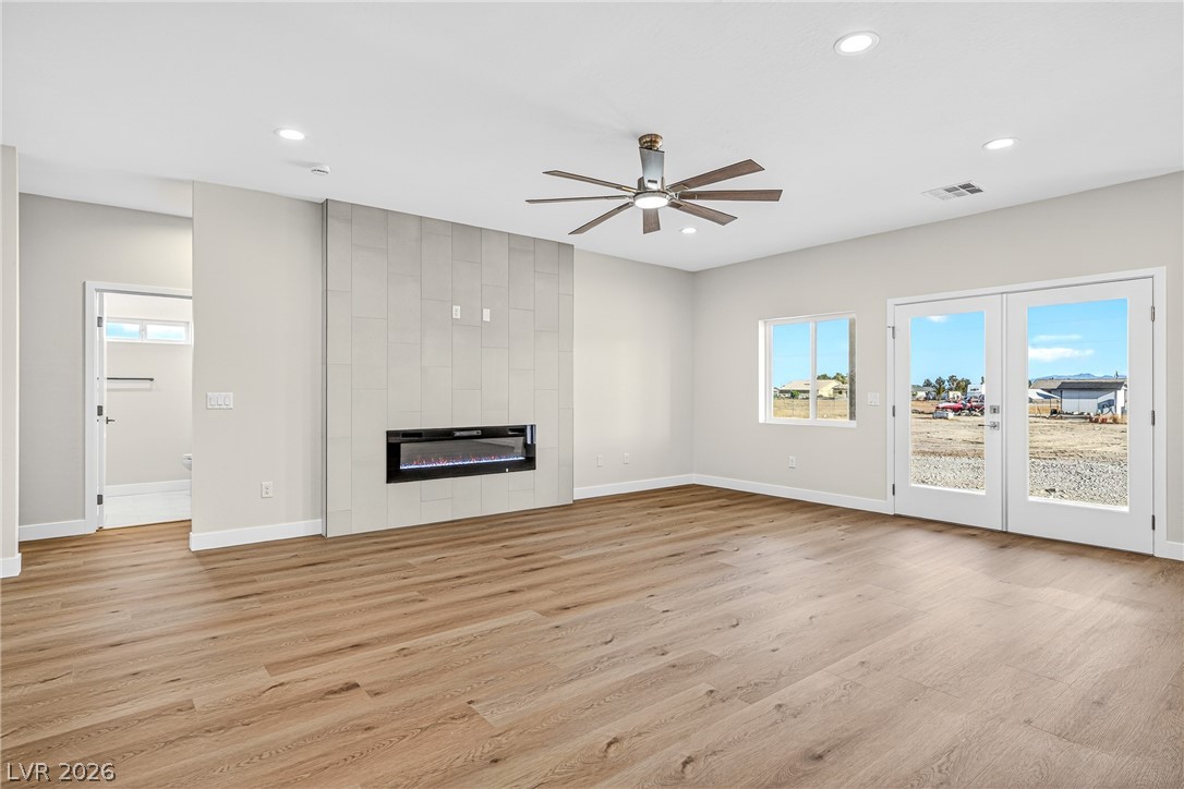 Empty living room with a tiled fireplace wall, wood-look floors, and glass double doors.