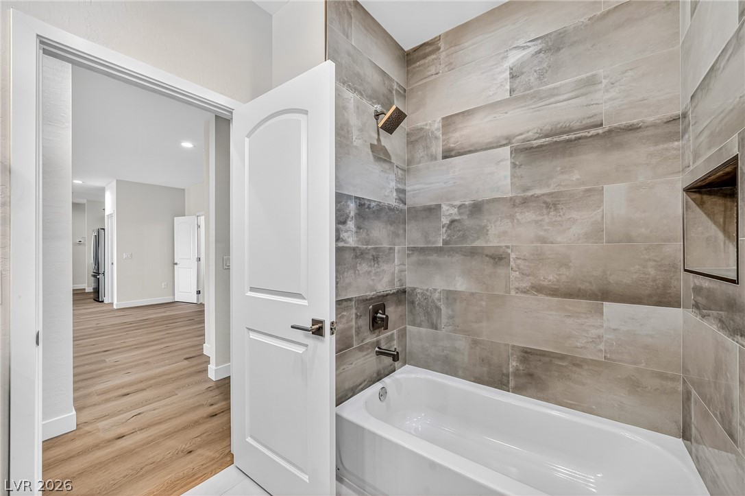Bathroom with a white bathtub, large tiled shower walls, and an open doorway to wood-look flooring.