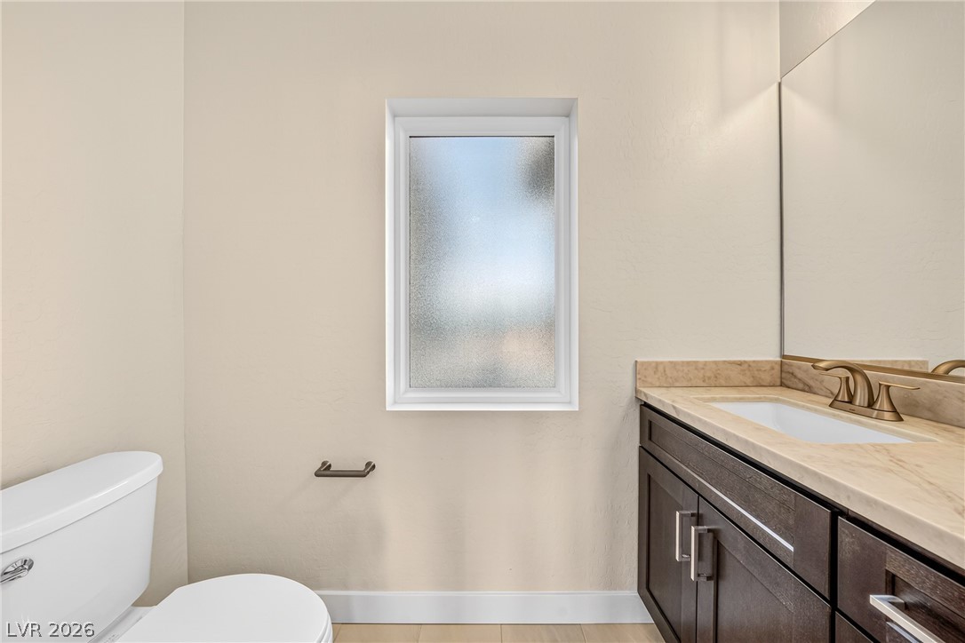 Bathroom with a dark wood vanity, beige countertop, and frosted window beside the toilet.