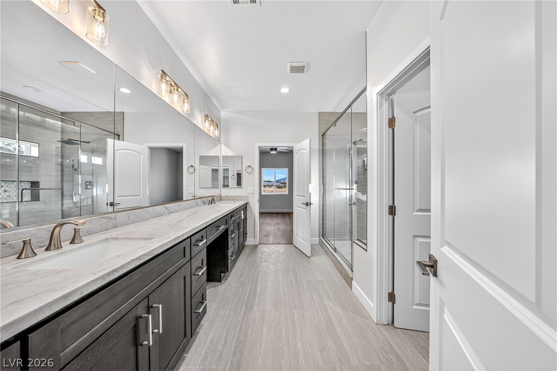 Modern bathroom with a long double vanity, mirrored wall, and glass-enclosed gray-tile showers.