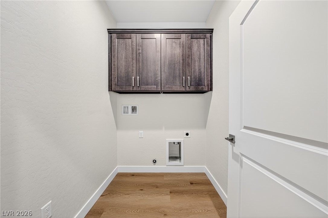 Empty laundry room with dark wood cabinets, appliance hookups, and wood-look flooring.