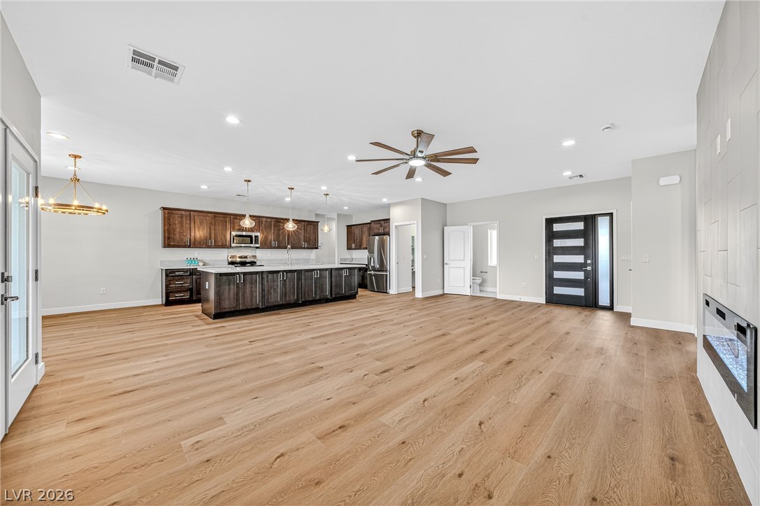 Open-plan kitchen with dark wood cabinets, a large island, light wood floors, and a built-in fireplace.