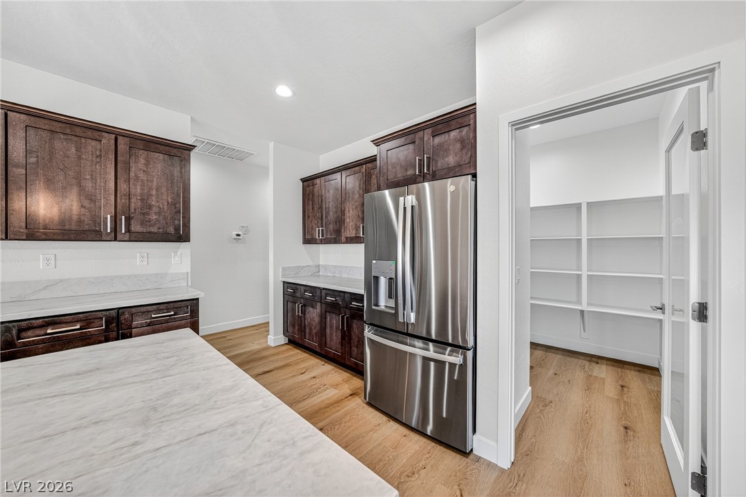 Kitchen with dark wood cabinets, marble-look counters, stainless steel refrigerator, and open pantry doorway.