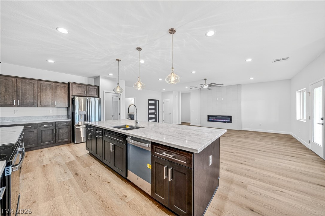 Open-plan kitchen with a large stone island, dark cabinets, stainless steel appliances, and an adjacent living area.
