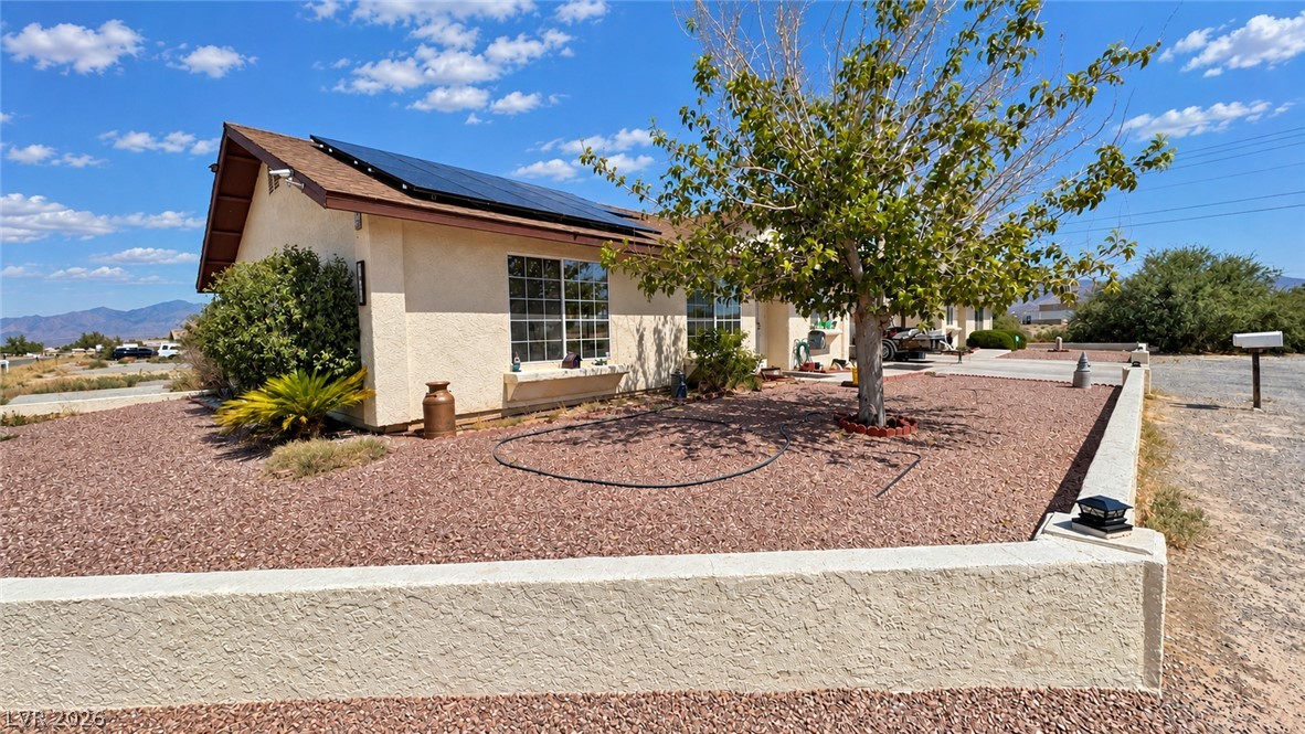 Single-story stucco home with rooftop solar panels, gravel landscaping, and distant mountains.