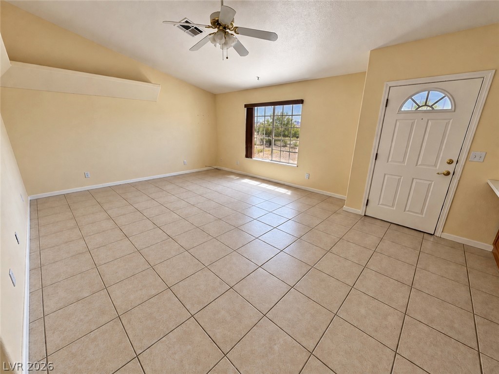 Empty living room with tiled floor, ceiling fan, and window beside the front door.