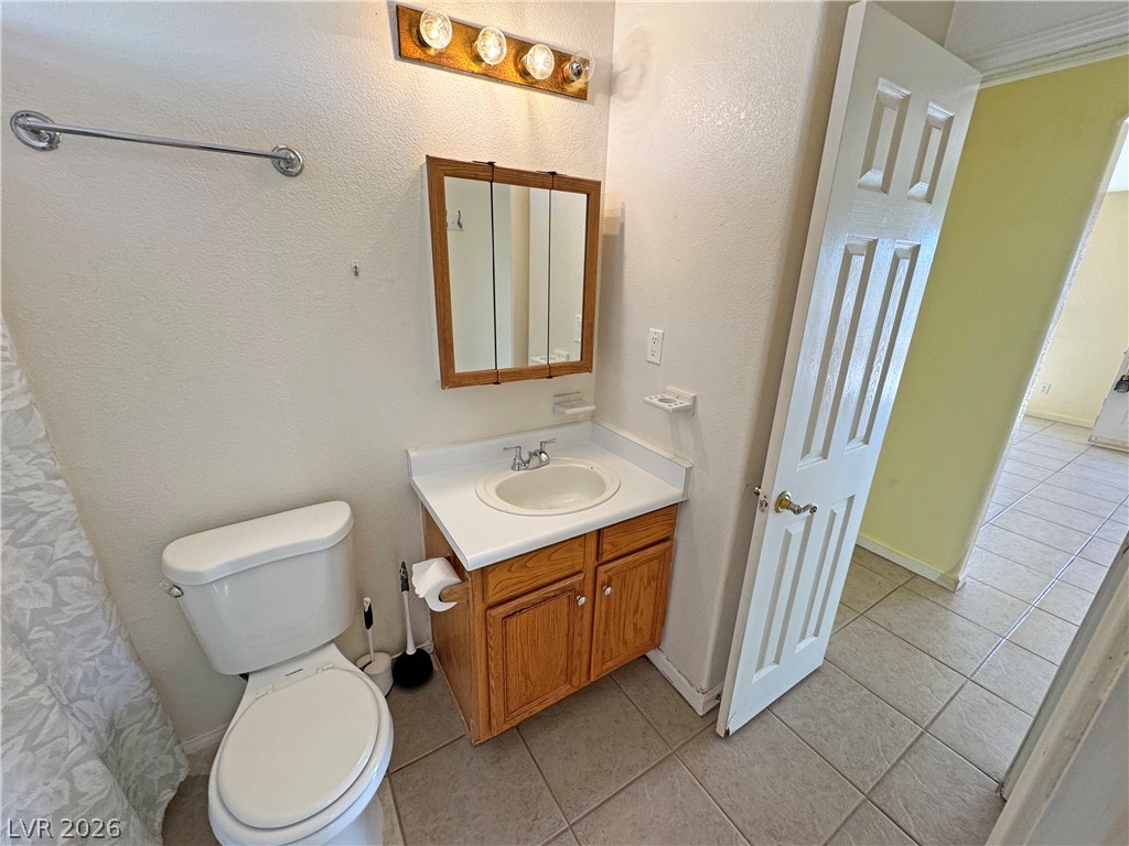 Bathroom with a wood vanity, mirrored medicine cabinet, and open door to a tiled adjoining room.