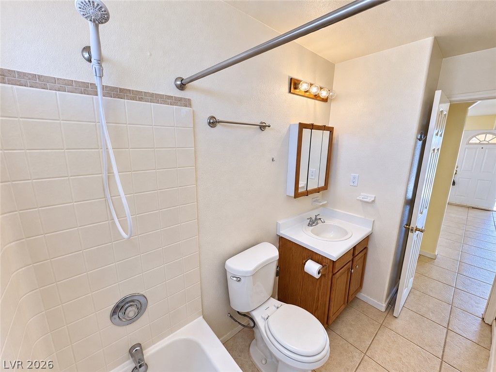 Bathroom with tiled tub and shower, wooden vanity, toilet, and grab bars.