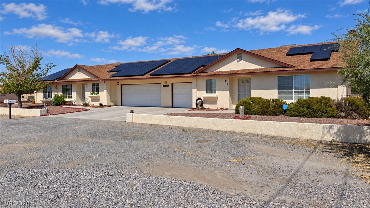 Single-story stucco home with rooftop solar panels, multiple garages, and a broad gravel driveway.