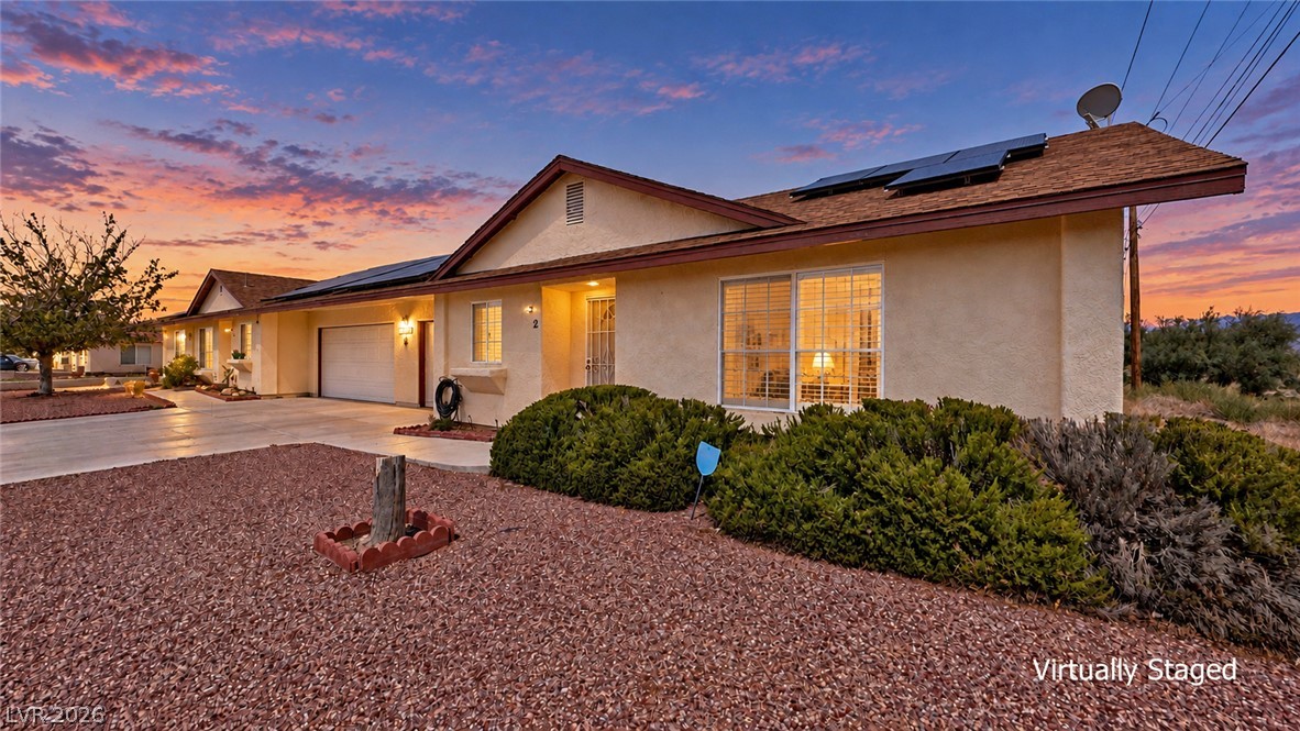 Single-story stucco home at dusk with solar panels, a two-car garage, and desert landscaping.