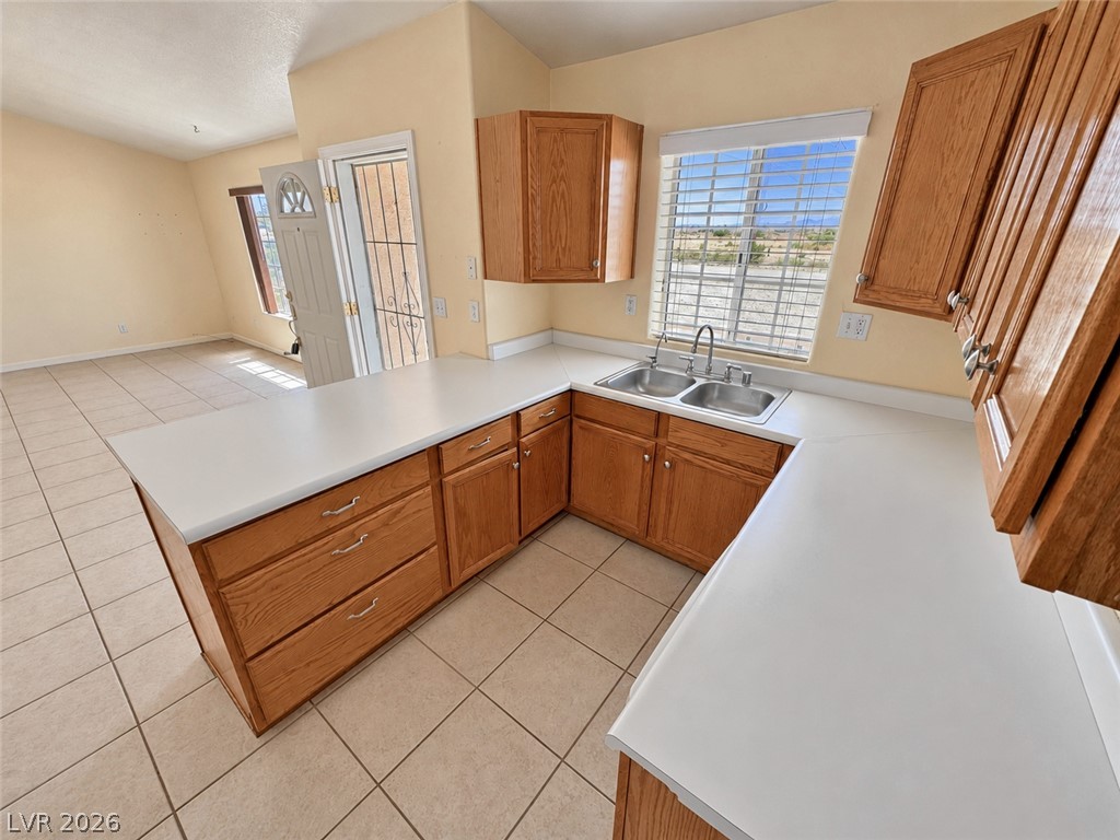 Empty kitchen with honey-colored cabinets, white countertops, and a double-basin sink beneath a window.